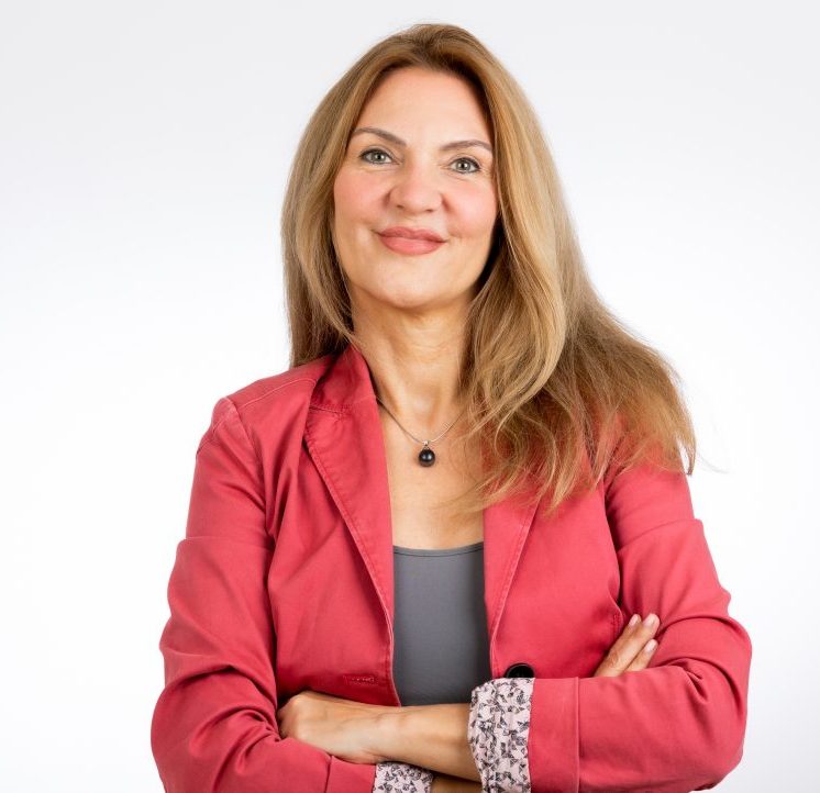Corina Hinsch Solutions - Professionelle HR Lösungen Frau mit langen, braunen Haaren, trägt eine rote Jacke und steht mit verschränkten Armen.